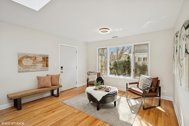 sitting room featuring a skylight, visible vents, baseboards, and light wood finished floors