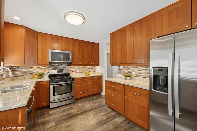 kitchen with stainless steel appliances, dark wood finished floors, a sink, and light stone counters