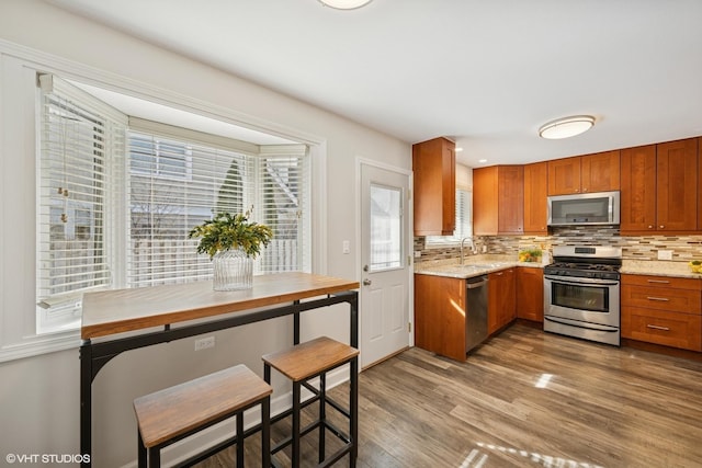 kitchen featuring tasteful backsplash, appliances with stainless steel finishes, brown cabinetry, a sink, and wood finished floors