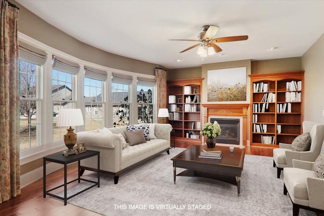 living room with ceiling fan, wood finished floors, a glass covered fireplace, and baseboards