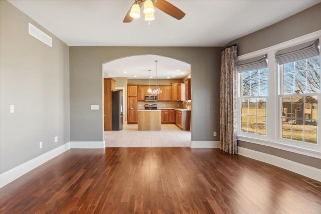 unfurnished living room with arched walkways, light wood-style flooring, a sink, visible vents, and baseboards