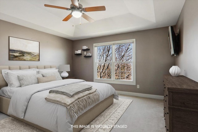 bedroom featuring light carpet, baseboards, a tray ceiling, and ceiling fan