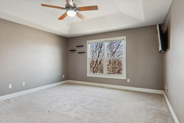 unfurnished room with ceiling fan, a tray ceiling, light colored carpet, and baseboards