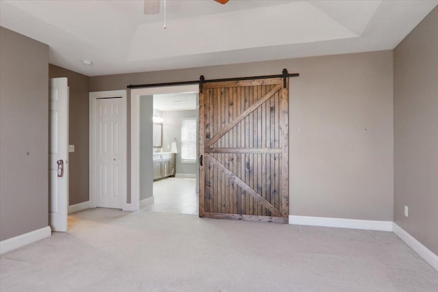 unfurnished room with a barn door, baseboards, a raised ceiling, ceiling fan, and carpet