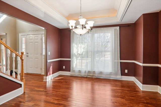 unfurnished dining area featuring a tray ceiling, crown molding, a notable chandelier, wood finished floors, and baseboards