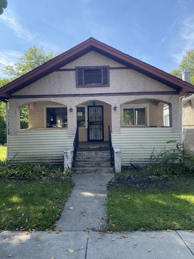 bungalow with a porch, a front yard, and stucco siding