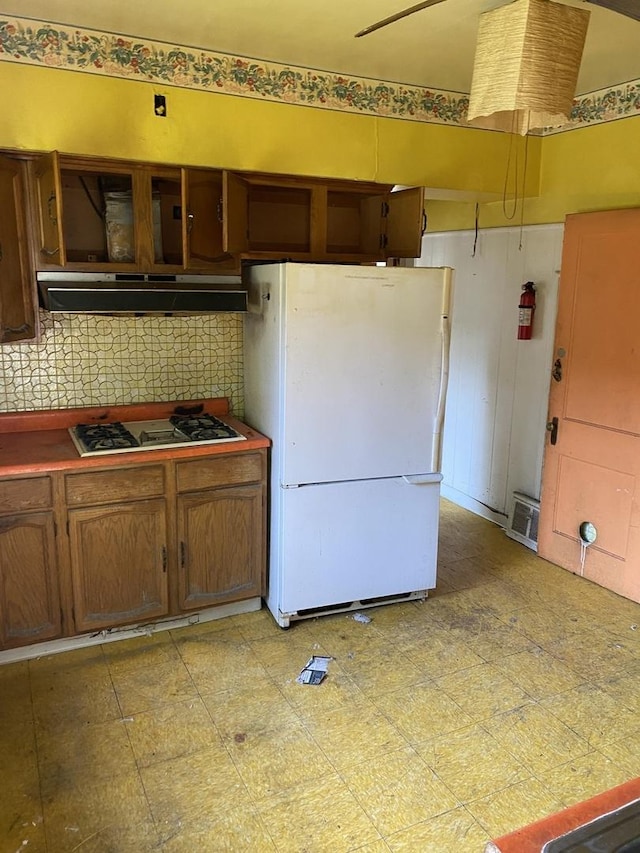 kitchen with under cabinet range hood, gas stovetop, freestanding refrigerator, light floors, and tasteful backsplash