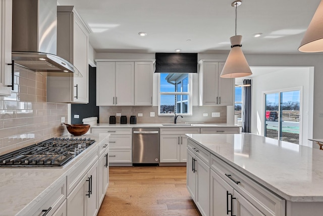 kitchen featuring white cabinets, light wood-style flooring, wall chimney exhaust hood, decorative light fixtures, and stainless steel appliances