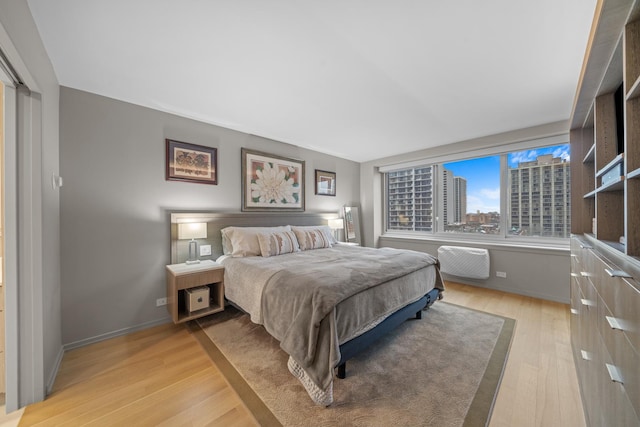 bedroom featuring a city view, light wood-style flooring, and baseboards