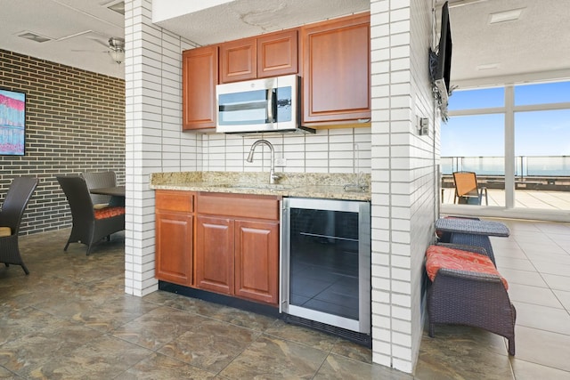 kitchen with a textured ceiling, beverage cooler, a sink, a ceiling fan, and stainless steel microwave