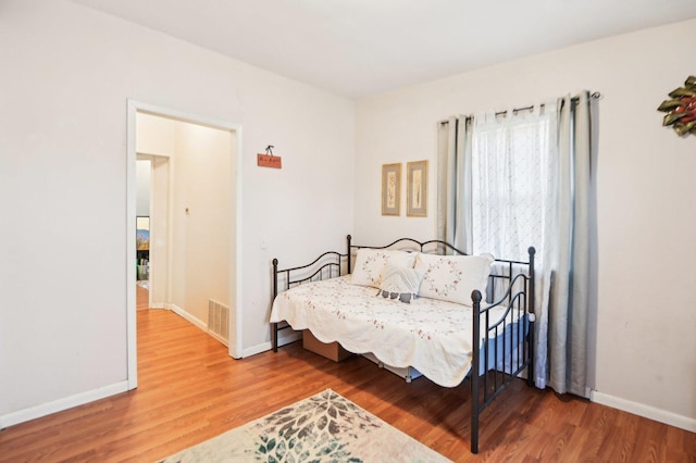 bedroom with baseboards, visible vents, and wood finished floors