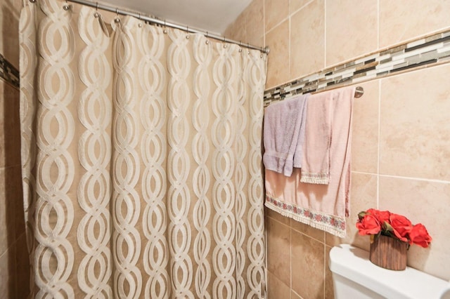 bathroom with toilet, a shower with curtain, and tile walls