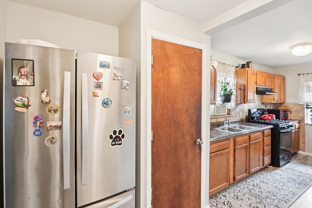 kitchen with tasteful backsplash, black gas range, freestanding refrigerator, a sink, and under cabinet range hood