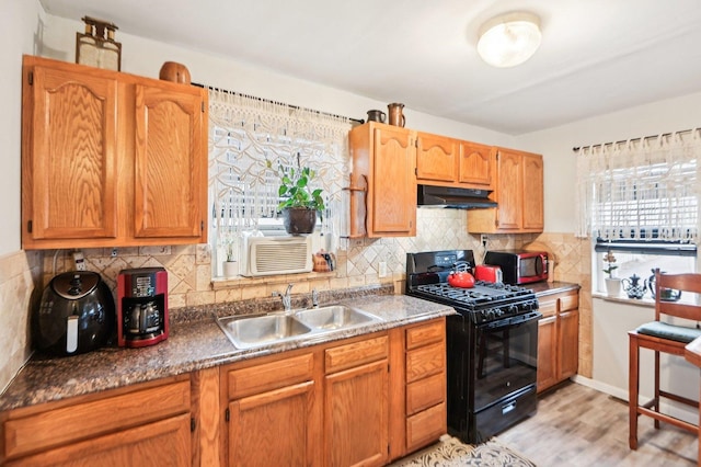 kitchen featuring black gas range, light wood-style floors, a sink, under cabinet range hood, and backsplash