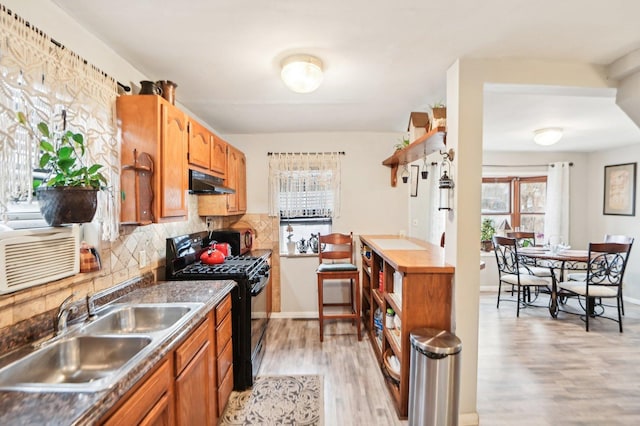 kitchen featuring black gas range oven, backsplash, a sink, light wood-type flooring, and under cabinet range hood