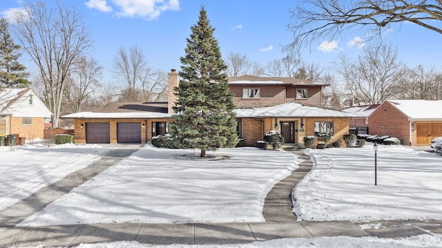 view of front of house featuring driveway, brick siding, a chimney, and an attached garage