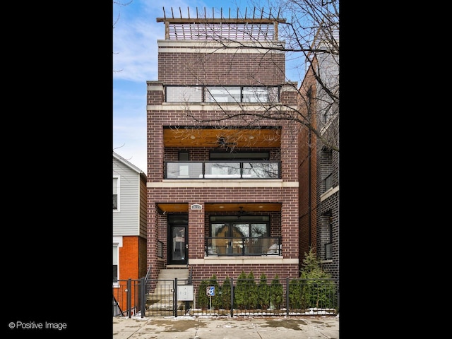 view of front of property featuring a fenced front yard, a gate, brick siding, and a balcony