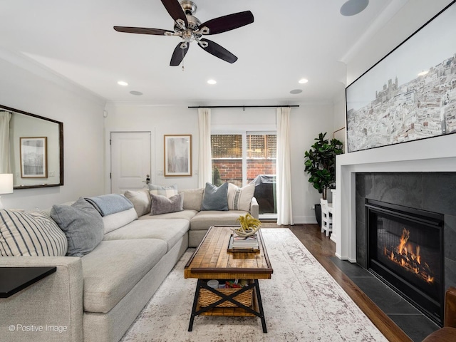 living room featuring a ceiling fan, dark wood-style floors, a fireplace with flush hearth, ornamental molding, and recessed lighting