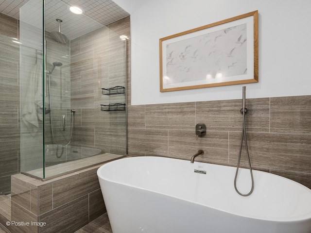 full bath featuring a shower stall, tile walls, and a freestanding bath