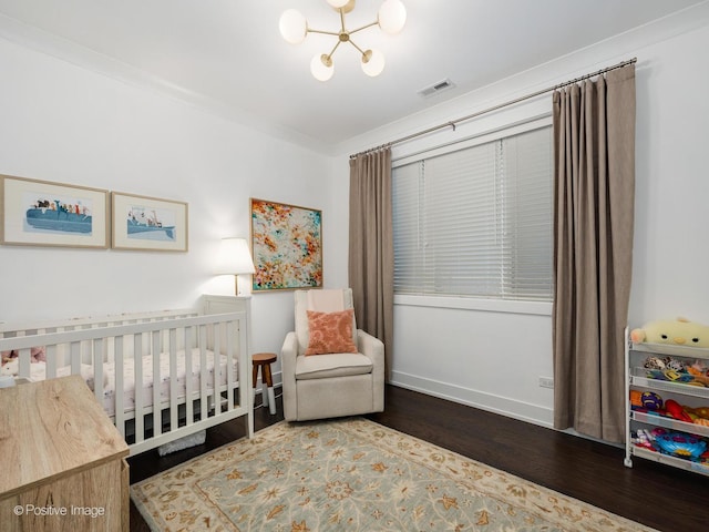 bedroom with a notable chandelier, visible vents, wood finished floors, a crib, and baseboards