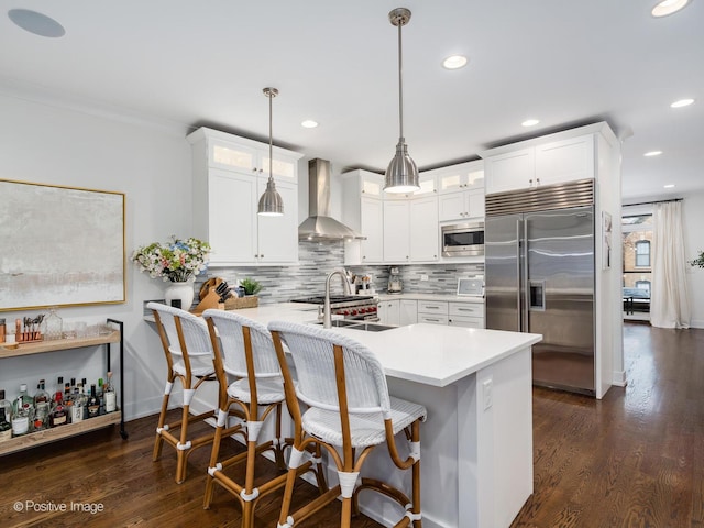 kitchen featuring wall chimney range hood, glass insert cabinets, backsplash, and built in appliances