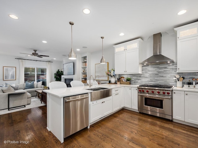 kitchen featuring a peninsula, stainless steel appliances, a sink, light countertops, and wall chimney exhaust hood