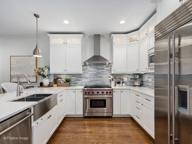 kitchen featuring decorative backsplash, wall chimney exhaust hood, built in appliances, hanging light fixtures, and white cabinetry