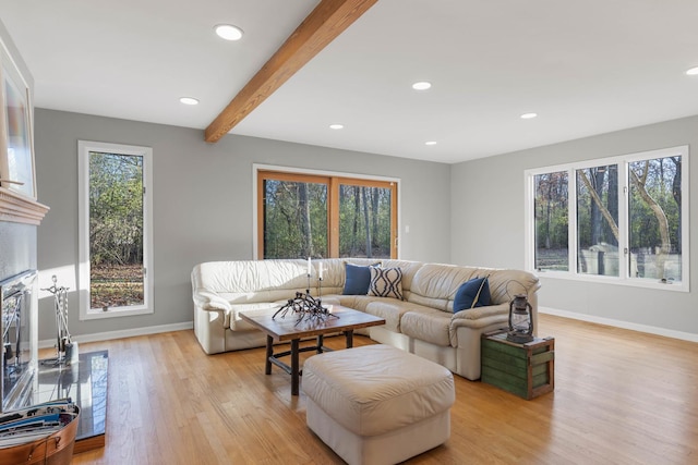 living area featuring light wood-style floors, beamed ceiling, a fireplace with flush hearth, and a healthy amount of sunlight