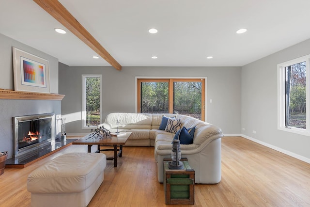 living area featuring light wood finished floors, a glass covered fireplace, beam ceiling, and baseboards