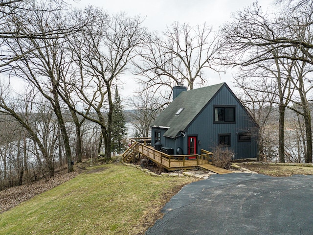 view of front of home featuring a deck, stairway, roof with shingles, a chimney, and a front yard