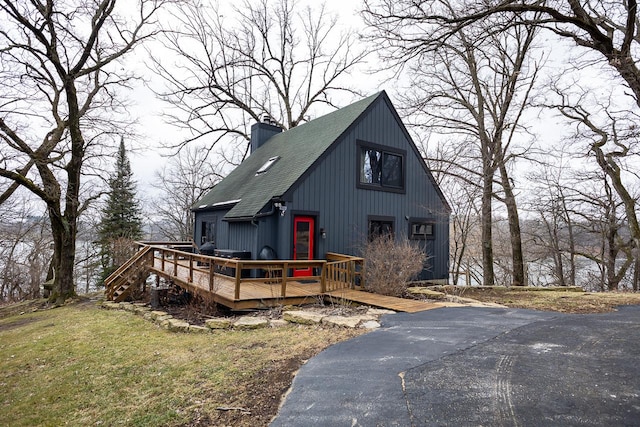 view of front of property featuring a shingled roof, a front yard, a chimney, and a deck