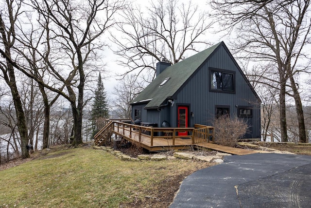 view of front of home with a shingled roof, a front yard, a chimney, and a wooden deck