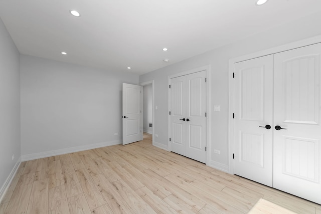 unfurnished bedroom featuring baseboards, light wood finished floors, two closets, and recessed lighting