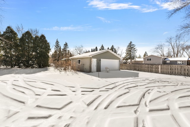 yard covered in snow featuring a garage, an outdoor structure, and fence