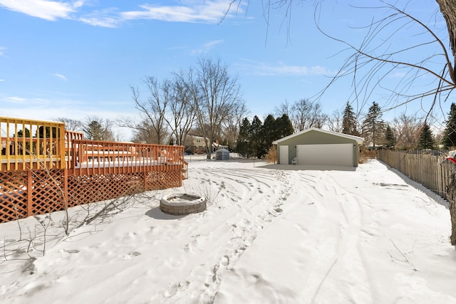 snowy yard with a garage, a fire pit, fence, a deck, and an outdoor structure