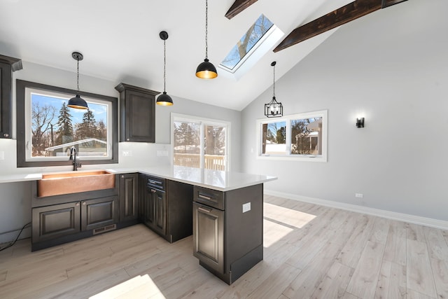 kitchen featuring a skylight, light countertops, light wood-style floors, a sink, and a peninsula