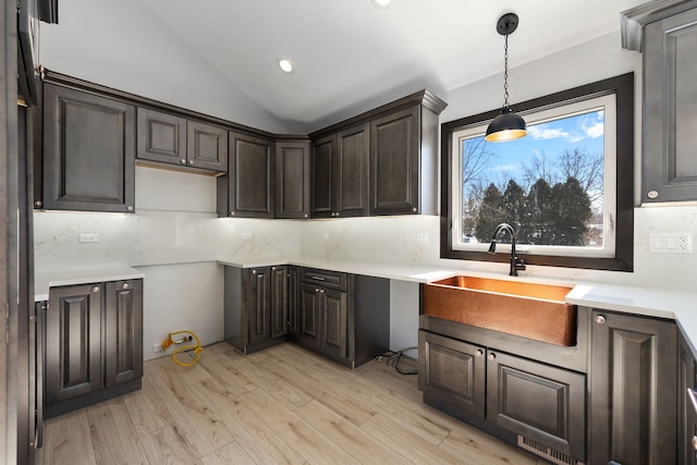 kitchen featuring a sink, vaulted ceiling, light countertops, light wood-type flooring, and decorative backsplash