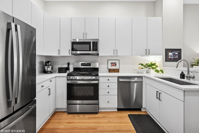 kitchen featuring tasteful backsplash, white cabinets, appliances with stainless steel finishes, light countertops, and a sink