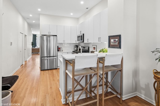 kitchen featuring a peninsula, white cabinetry, light countertops, appliances with stainless steel finishes, and a kitchen bar