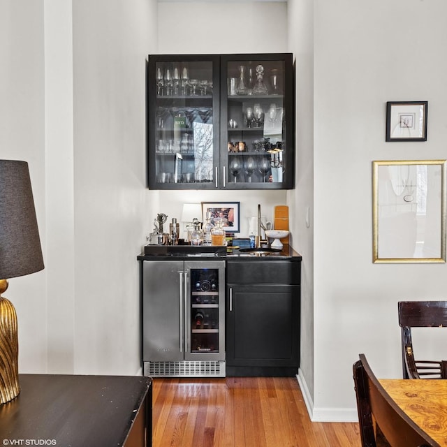 bar featuring wine cooler, a sink, wood finished floors, baseboards, and a dry bar