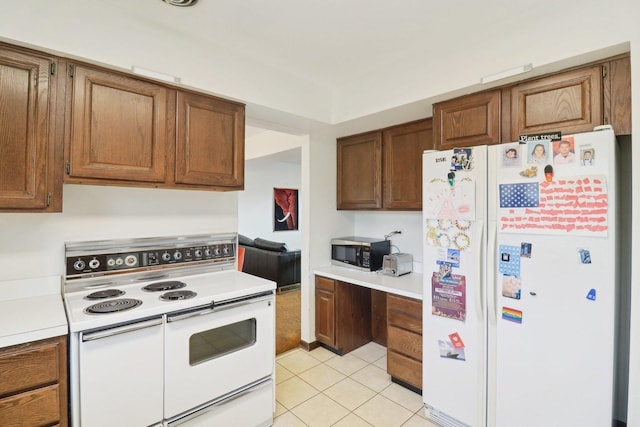 kitchen featuring brown cabinets, built in desk, light tile patterned floors, light countertops, and white appliances