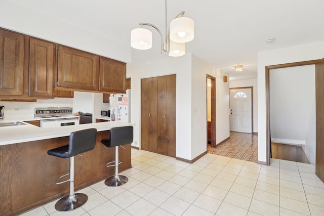 kitchen with light tile patterned floors, decorative light fixtures, light countertops, white electric range, and a sink