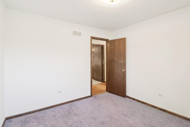 empty room featuring light carpet, visible vents, and baseboards