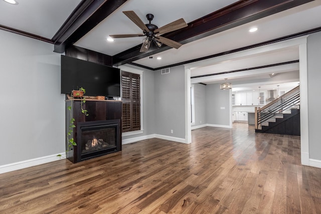 living area featuring crown molding, visible vents, a glass covered fireplace, wood finished floors, and beamed ceiling