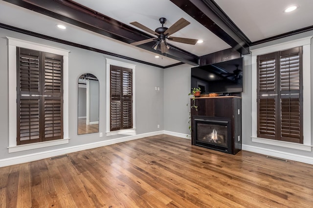 unfurnished living room featuring ornamental molding, a glass covered fireplace, beamed ceiling, and wood finished floors