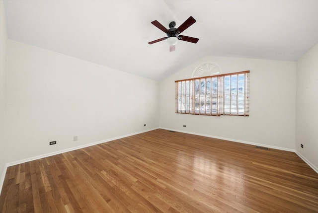 empty room featuring lofted ceiling, visible vents, baseboards, and wood finished floors