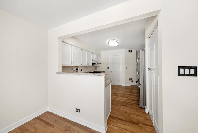 kitchen with baseboards, decorative backsplash, wood finished floors, freestanding refrigerator, and white cabinetry