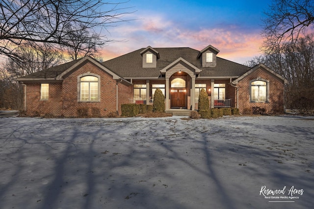 view of front of house featuring covered porch, a shingled roof, and brick siding