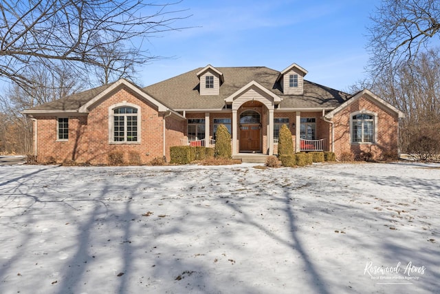 view of front of home featuring covered porch, brick siding, and a shingled roof