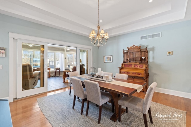 dining space with light wood finished floors, visible vents, baseboards, a tray ceiling, and recessed lighting